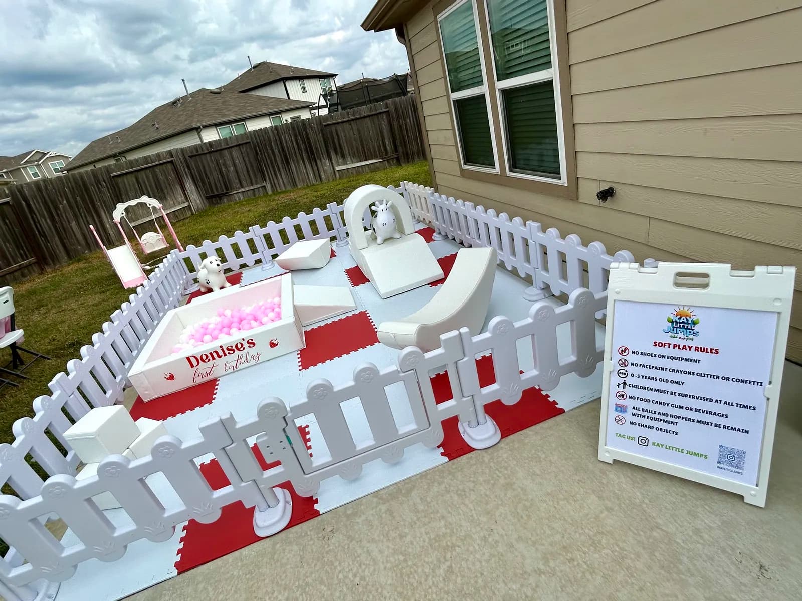 Backyard soft play on red and white mats with a personalized ball pit and unicorn rocker